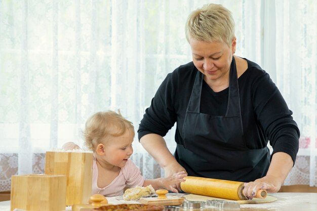 Una bellissima bambina sorridente aiuta la nonna a stendere la pasta per biscotti.