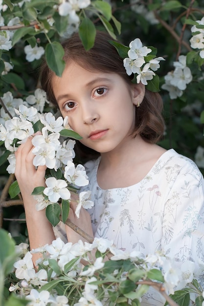 Una bellissima bambina tra il fogliame verde e i fiori bianchi dei meli in fiore Giornata di primavera Un bambino felice sorride e guarda la telecamera