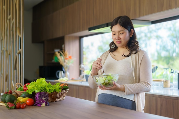 Una bellissima donna incinta asiatica prepara felicemente un'insalata di verdure, cibo biologico e sano.