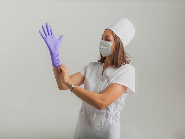 Una bellissima dottoressa o infermiera con una maschera protettiva e guanti di gomma su uno sfondo chiaro con copyspace. Concetto di assistenza sanitaria