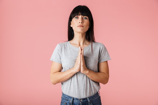 una bellissima e straordinaria donna nervosa emotiva in posa isolata su un muro rosa chiaro che mostra un gesto di speranza per favore.