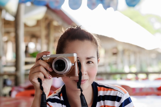 Una bellissima fotografa asiatica sta sollevando una fotocamera digitale fissata all'occhio destro per registrare immagini.