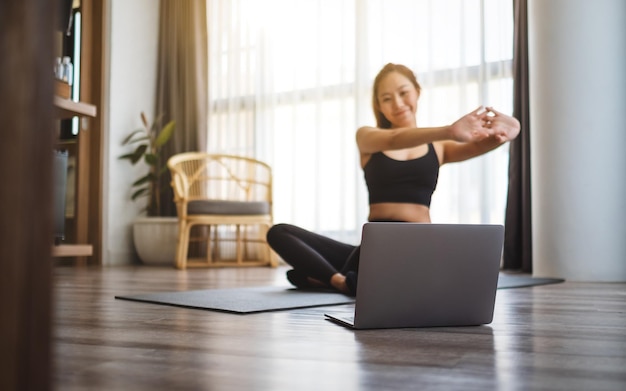 Una bellissima giovane donna asiatica che allunga le braccia mentre guarda tutorial di allenamento online sul laptop a casa