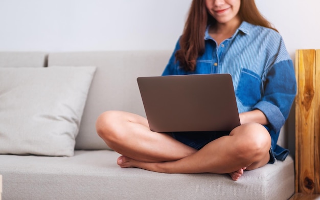 Una bellissima giovane donna che utilizza e lavora al computer portatile mentre è seduta su un divano a casa