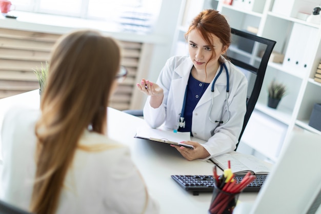 Una bellissima giovane donna in abito bianco è seduta alla scrivania in ufficio e sta comunicando con l'interlocutore.