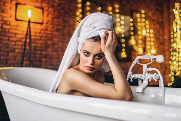 Una bellissima giovane donna in posa in studio. Donna sdraiata in una vasca da bagno bianca con un asciugamano in testa.
