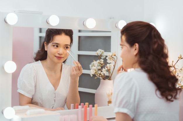 Una bellissima giovane donna seduta a un tavolo da trucco e facendo il suo trucco.