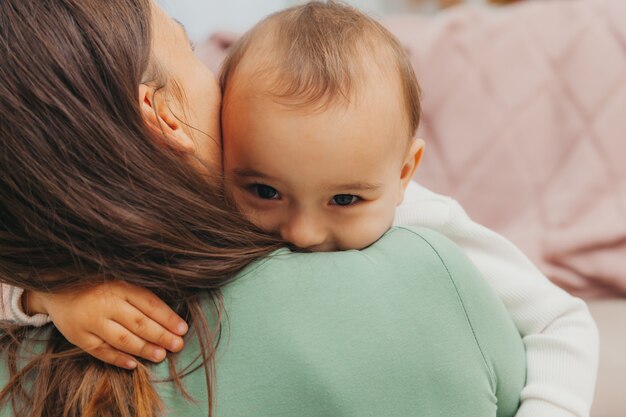 Una bellissima giovane madre è seduta sul pavimento del soggiorno e abbraccia il suo piccolo bambino. Una famiglia felice.