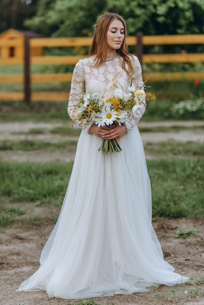 Una bellissima giovane sposa con un mazzo di margherite in un campo