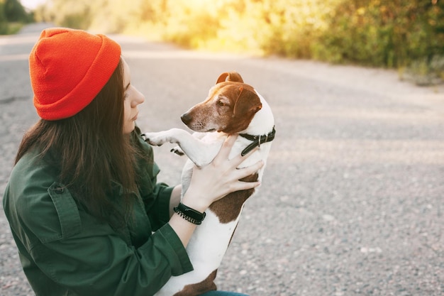 Una bellissima ragazza con un cappello arancione tiene il suo cane tra le braccia la ragazza si prende cura del suo animale domestico