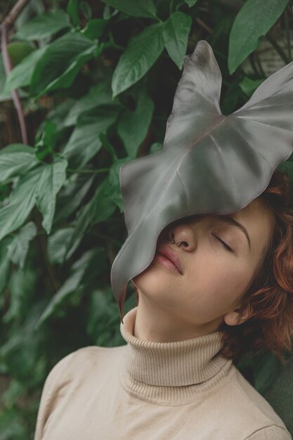 Una bellissima ragazza plus size con i capelli rossi tra i rami verdi delle piante tropicali