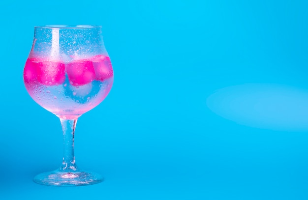 Una bevanda fredda con ghiaccio colorato rosa e blu in un bicchiere di vino su uno sfondo blu