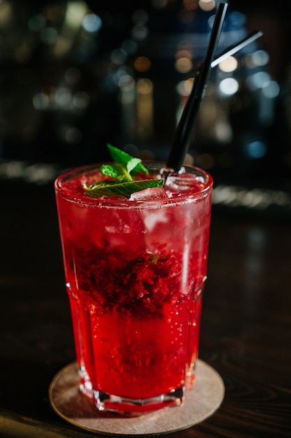 Una bevanda rossa in un bicchiere con cubetti di ghiaccio, fragole, paglia e foglie di menta