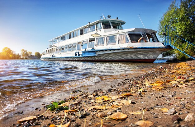 Una bianca motonave da diporto si trova sulla riva del Volga e le foglie d'autunno giacciono vicino all'acqua