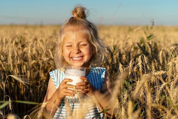 Una bimba bionda in un campo di segale sorride, un bambino felice nelle orecchie con un bicchiere di latte