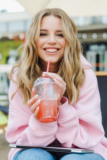 Una bionda in abiti eleganti beve un cocktail sulla terrazza di un caffè di strada La modella si sta godendo la vita