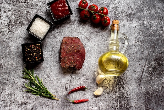 Una bistecca, aglio e olio d'oliva sono disposti su uno sfondo grigio.