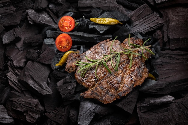 Una bistecca con un rametto di rosmarino sopra del carbone nero