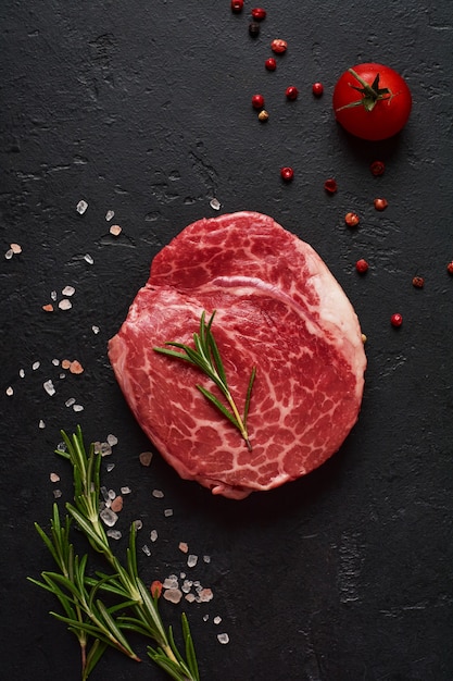 Una bistecca cruda parigina fresca su carta pergamena bianca con sale, pepe e rosmarino in stile rustico su fondo di pietra vecchia. Black angus. Vista dall'alto.