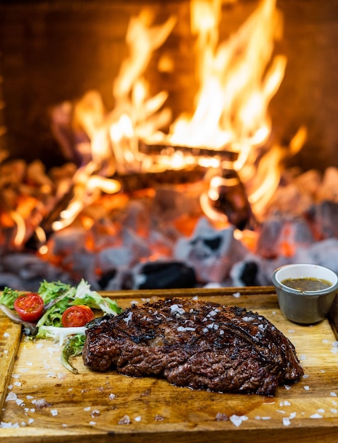 una bistecca e una ciotola di insalata sono su un tavolo davanti al fuoco