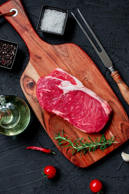 Una bistecca su un tagliere con un bicchiere di vino e una bottiglia di peperoncino.