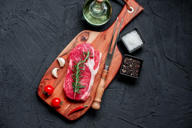 Una bistecca su una tavola di legno con un coltello e una bottiglia di sale e pepe.