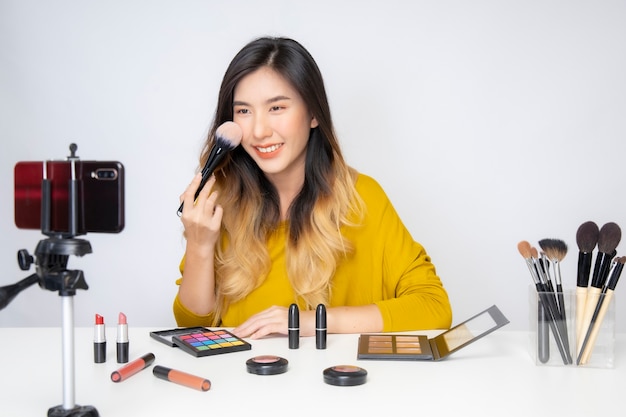 Una blogger asiatica di bellezza che gira un video in cui indossa un rossetto arancione in uno studio.