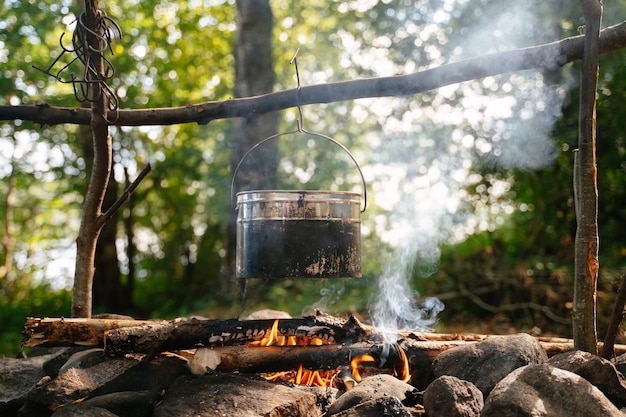 una bombetta turistica coperta di fuliggine pende sopra un falò fumante in un accampamento nella foresta in estate