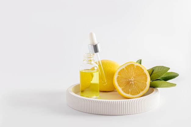 Una bottiglia aperta con un siero idratante illuminante o un olio di limone cosmetico riempito con una pipetta su un vassoio bianco uno spazio per le copie