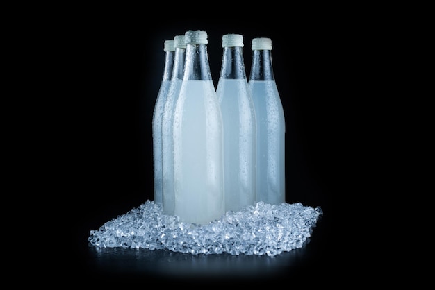 Una bottiglia bianca con una bibita gassata su ghiaccio su sfondo nero