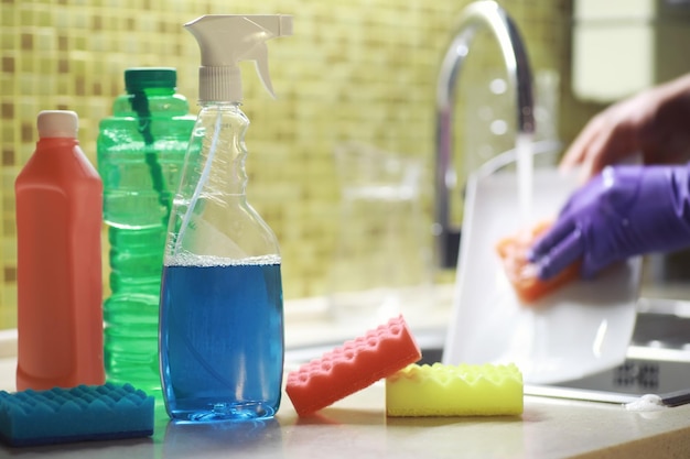 Una bottiglia con un detersivo per piatti ecologico sullo sfondo di una casalinga che lava i piatti