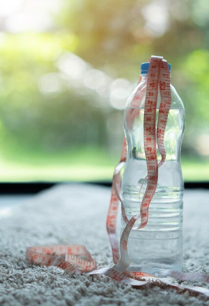 Una bottiglia di acqua ferma e un nastro di misurazione su un tappeto grigio con sfondo naturale