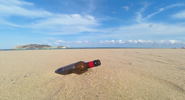 Una bottiglia di birra sulla spiaggia con un cielo nuvoloso e blu