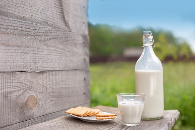 Una bottiglia di latte fresco, un bicchiere e un piattino con cracker su un tavolo di legno che si affaccia a