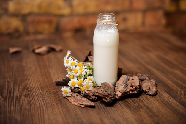 Una bottiglia di latte rustico e un bouquet di camomilla su un tavolo di legno