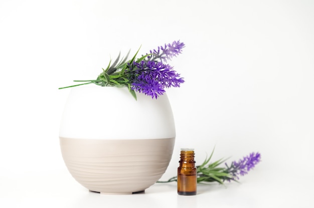 Una bottiglia di olio aromatico un diffusore e lavanda su sfondo bianco