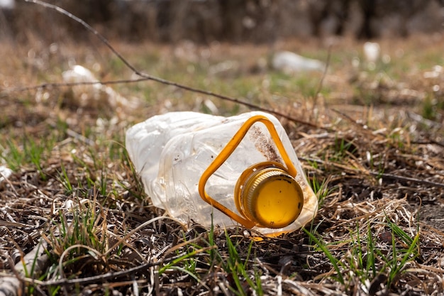 Una bottiglia di plastica con un tappo giallo gettata in natura sull'erba