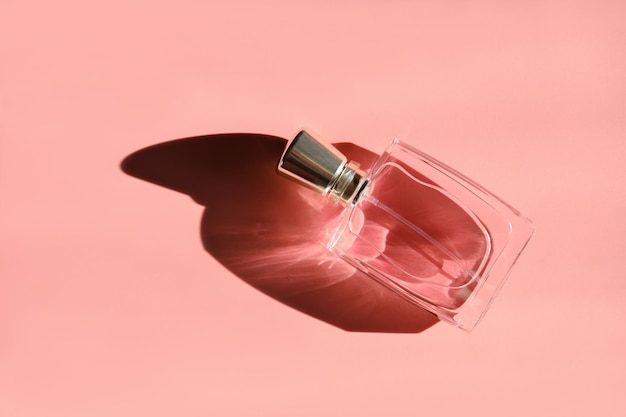 Una bottiglia di profumo con luce diretta e lunghe ombre colorate su sfondo rosa in stile minimalista