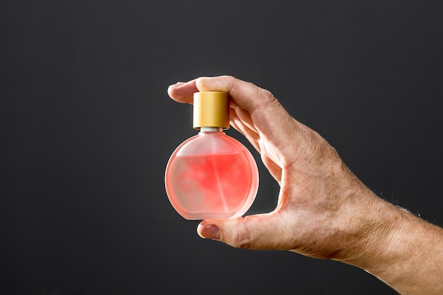 Una bottiglia di profumo da donna nella mano di un uomo su sfondo nero