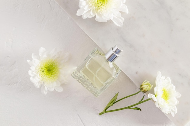 Una bottiglia di profumo femminile con una fragranza floreale è rivestita su piastrelle di marmo con fiori bianchi concetto alla moda di materiali naturali e aroma