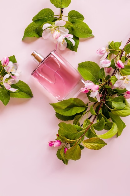 Una bottiglia di profumo o spray da donna giace su uno sfondo rosa tra i rami di un melo in fiore leggero aroma di prodotto cosmetico