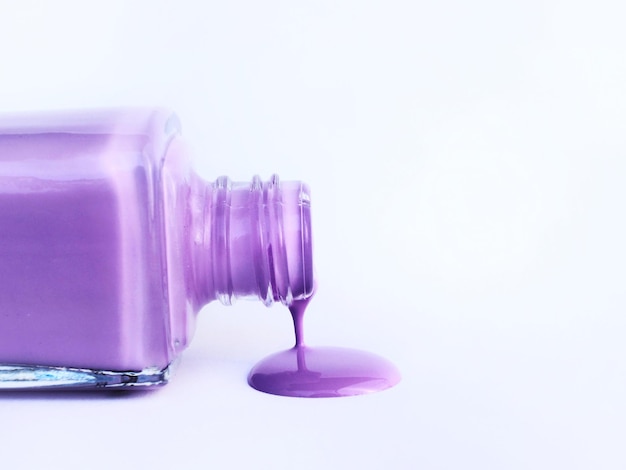 Una bottiglia di smalto viola viene versata su uno sfondo bianco