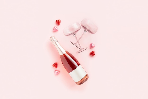Una bottiglia di vino frizzante con due bicchieri e caramelle al cioccolato a forma di cuore su sfondo rosa