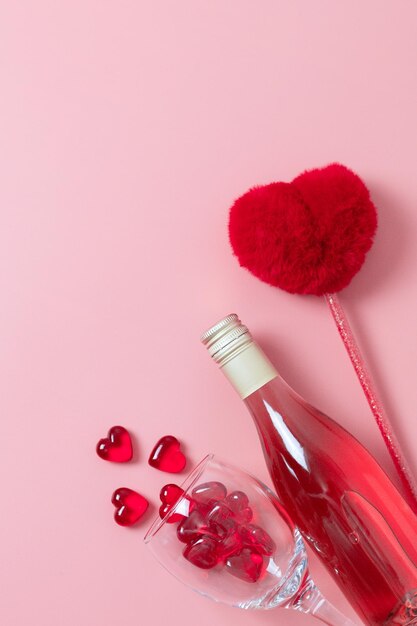 Una bottiglia di vino un bicchiere con cuori di vetro e una penna sul rosa