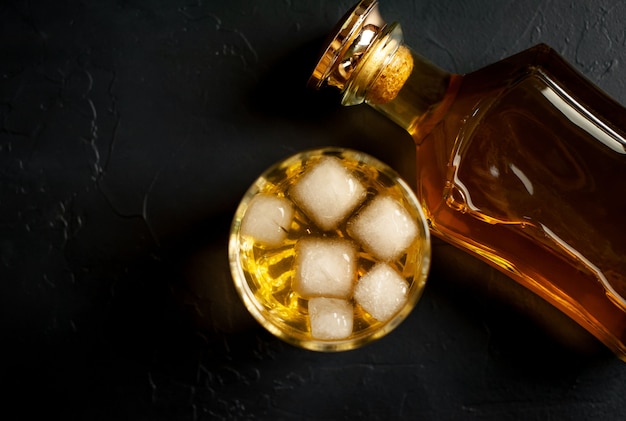 una bottiglia di whisky e un bicchiere di whisky con ghiaccio su cemento