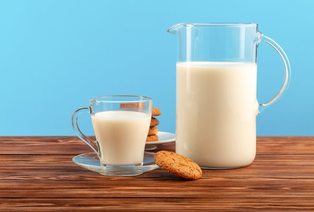 Una brocca e un bicchiere di latte con i biscotti sulla tavola di legno sul blu