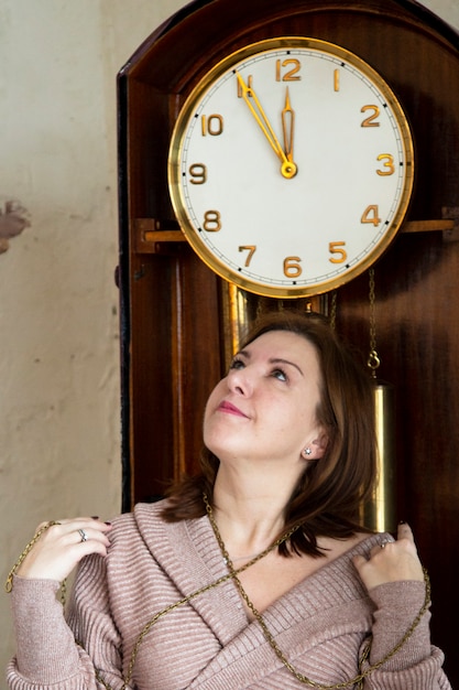 Una bruna accanto a un grande orologio a pendolo. Tempo di attesa.