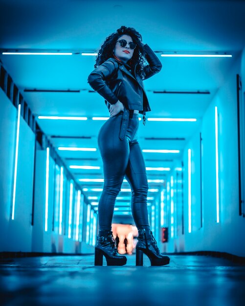 Una bruna dai capelli ricci con pelle e in un tunnel illuminato con leed blu