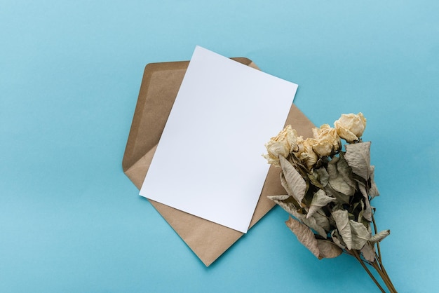 Una busta di carta kraft con una carta bianca bianca fiori su sfondo blu Preparazione della cartolina