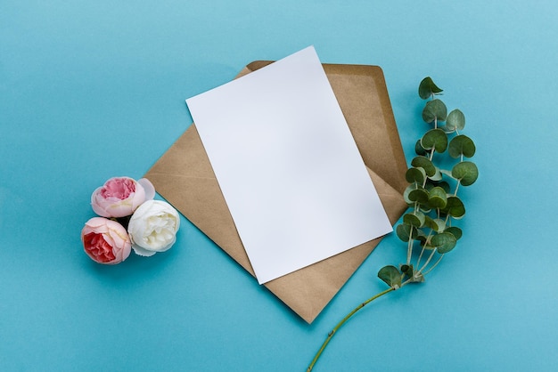 Una busta di carta kraft con una carta bianca bianca fiori su sfondo blu Preparazione della cartolina